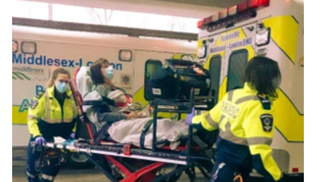 A scene from the case showing a masked woman on a stretcher being transported by two EMTs. There are two ambulances in the background.